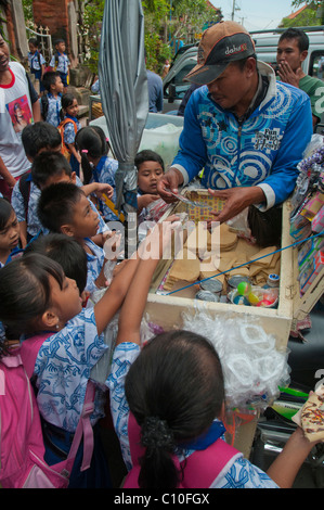 Indonesian primary school children buying after school treats from a street vendor outside their school in Ubud, Bali, Indonesia Stock Photo