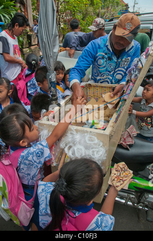 Indonesian primary school children buying after school treats from a street vendor outside their school in Ubud, Bali, Indonesia Stock Photo