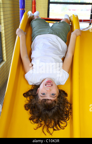 Brunette little girl upside down playground slide Stock Photo - Alamy