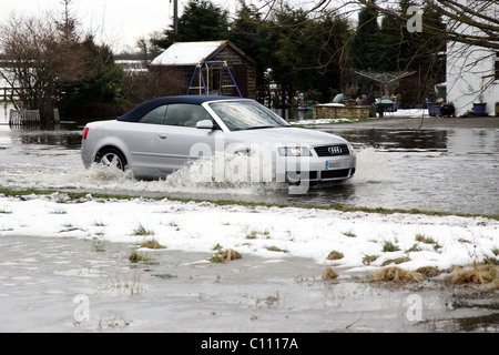 Motorists pass through floods caused by melting snow and ice on the roads in Cricklade near Swindon Wiltshire, England - Stock Photo