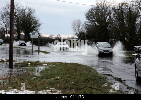 Motorists pass through floods caused by melting snow and ice on the roads in Cricklade near Swindon Wiltshire, England - Stock Photo