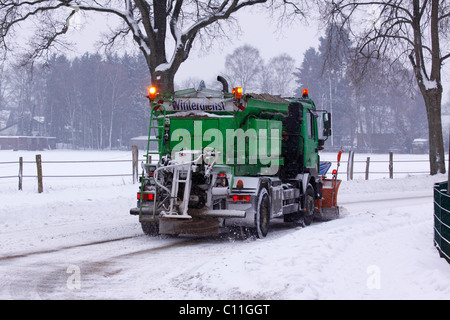 Snow-clearing vehicle clearing the road from snow and ice, spreading sand against black ice, Stock Photo