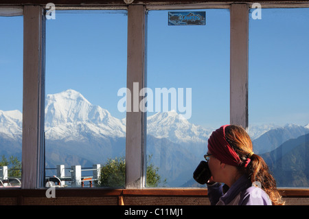 A trekker drinking tea in a lodge and looking at the mountains through the window. Nepal himalayas, annapurna from Ghorepani Stock Photo