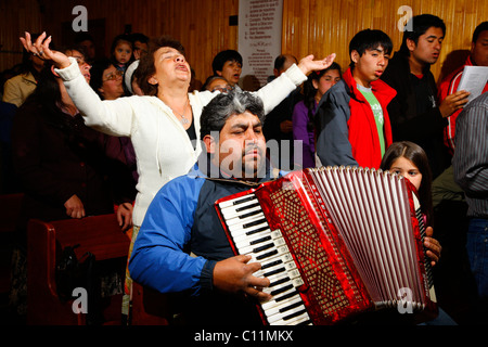 Man playing accordion, woman praying with her arms raised, during church service, mining town of Lota, Chile, South America Stock Photo