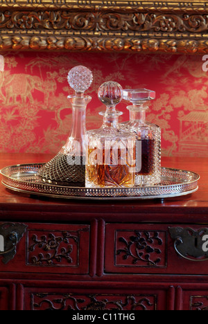 Liqueurs in antique crystal glass decanters on a silver tray and an Asian chest in a luxurious ambience Stock Photo
