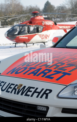 Rescue helicopter Christoph 41, identifier D-HDRC, landing on a snow-covered meadow, in front a Porsche Cayenne ambulance of the Stock Photo