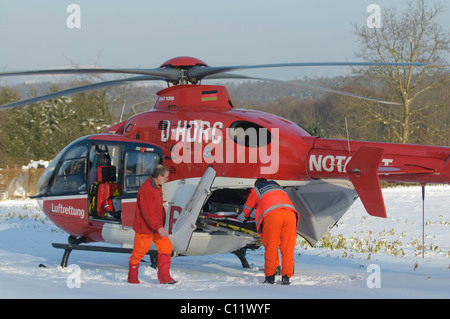 Rescue helicopter Christoph 41, identifier D-HDRC, landing on a snow-covered meadow, in front a Porsche Cayenne ambulance of the Stock Photo