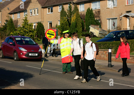 A Lollipop man doing his duty seeing school children across a busy road Stock Photo