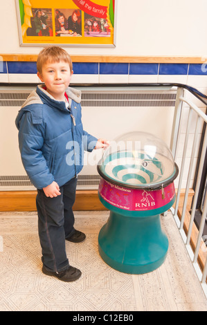 A MODEL RELEASED six year old boy puts money in a charity box for the Royal national Institute for the Blind in the Uk