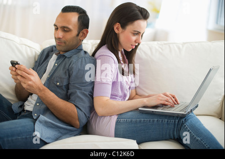 USA, New Jersey, Jersey City, couple sitting on sofa back to back using laptop and phone Stock Photo