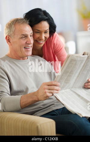 USA, New Jersey, Jersey City, Mature couple sitting in armchair, reading newspaper Stock Photo