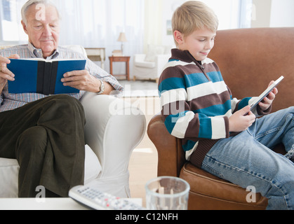 USA, New Jersey, Jersey City, grandfather reading book, grandson (8-9) reading e-book in living room Stock Photo
