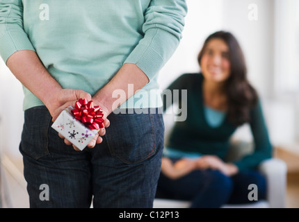 USA, New Jersey, Jersey City, Young man with present behind his back, girlfriend in background Stock Photo