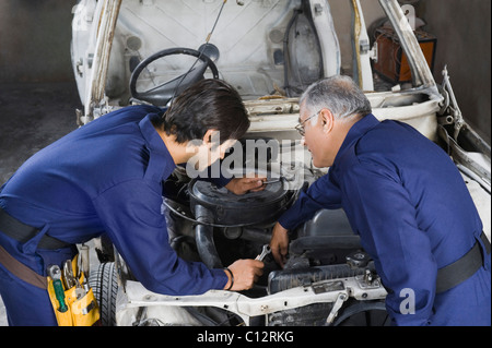 Auto mechanic with an apprentice repairing a car in a garage Stock Photo