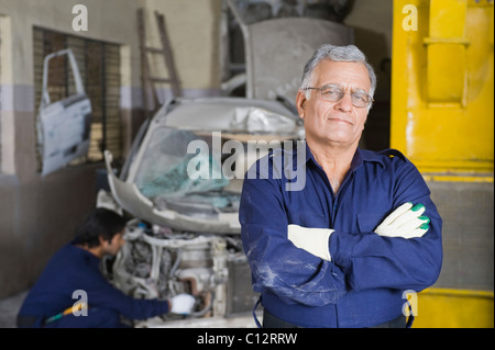 Portrait of an auto mechanic with an apprentice repairing a car in the background Stock Photo
