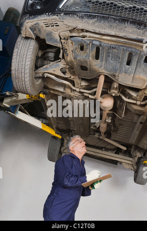 Car mechanic checking a car raised on a hydraulic lift Stock Photo - Alamy