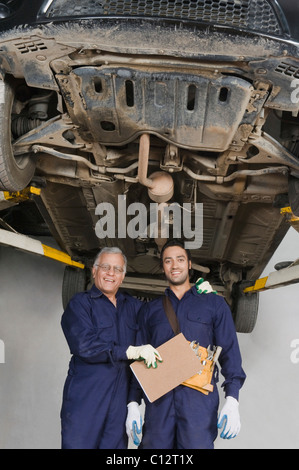 Auto mechanic with an apprentice standing under a raised car in a garage Stock Photo