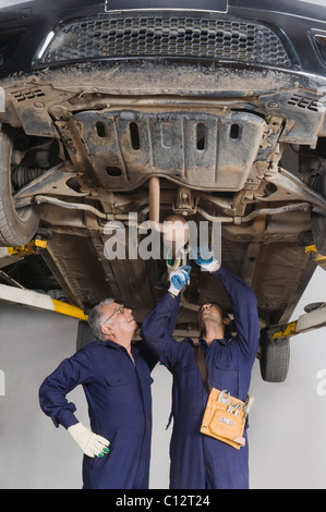 Auto mechanic with an apprentice working under a raised car in a garage Stock Photo