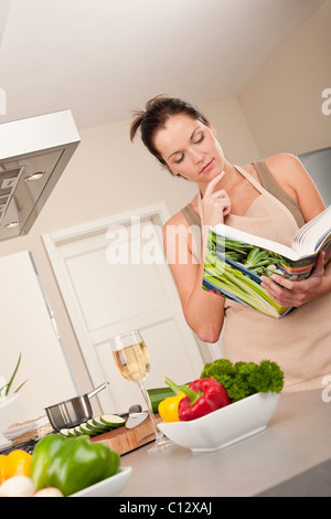Young woman reading cookbook in the kitchen, looking for recipe Stock Photo