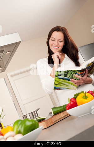 Young woman reading cookbook in the kitchen, looking for recipe Stock Photo