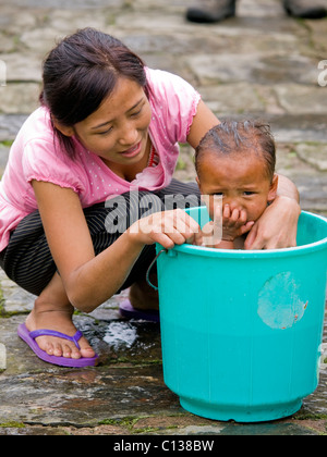 Young mother is washing her daughter in a small bucket Stock Photo