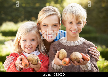Young mother and children in garden pose with vegetables Stock Photo