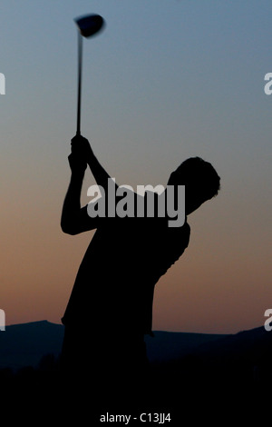 Man playing golf with a scenic landscape surrounding him as the sun sets Stock Photo