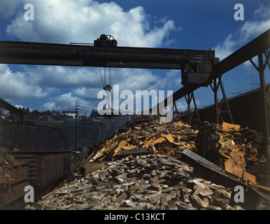 Recycling scrap steel during World War II at the Allegheny Ludlum Steel Corporation in Brackenridge, Pennsylvania. An overhead magnet deposits the scrap in a loader which carries it to the open-hearth furnace. 1941. Stock Photo