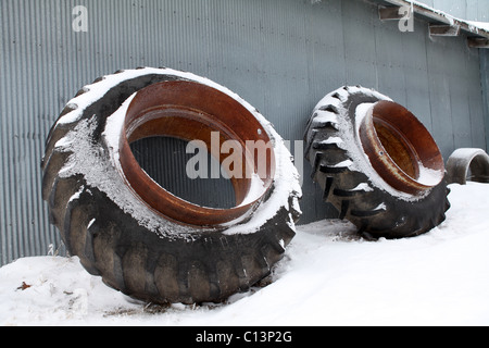 Large tractor tires with rim leaning on tin shed in snow Stock Photo