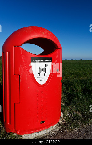 A bright red Dog Waste Bin next to a green field with a very blue sky. 7th March 2011 Stock Photo