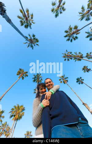 Couple hugging, looking at camera with sky and palm trees behind them.  Low angle POV.  Santa Barbara, California USA Stock Photo
