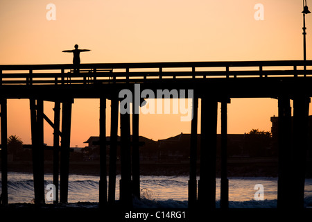 A silhouetted woman does a yoga pose on the Ventura Pier in Ventura, California. Stock Photo