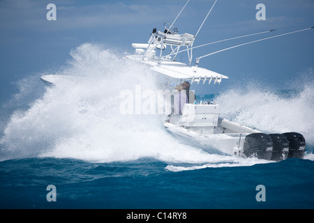 A fishing boat speeds through the blue surf spraying white water. Stock Photo