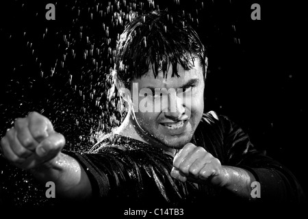 A young man wearing a jacket poses in a wushu stance while it rains down on him. Stock Photo