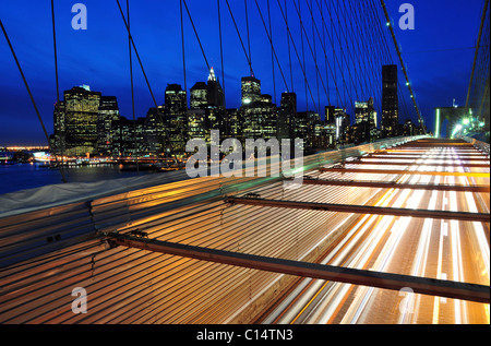 Cars pass over the Brooklyn Bridge with the New York City skyline in the background at dusk, New York.
