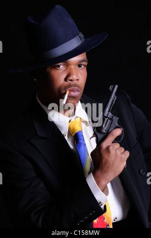 Young African American man posing as a gangster in a colorful tie, fedora and holding a revolver Stock Photo