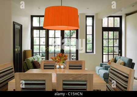 Large orange lampshade above wooden dining table in room with glass panelled windows Stock Photo