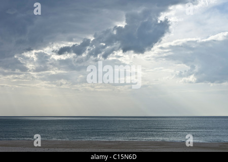 Dramatic lighting with shafts of light shining through the clouds over the Atlantic ocean in an empty beach Stock Photo