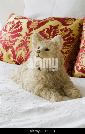 Cuddly dog toy on white bedding with baroque patterned cushions Stock Photo