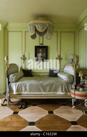 Antique bed with satin upholstered headboards and bolster cushions in Georgian style bedroom with green wall panelling Stock Photo