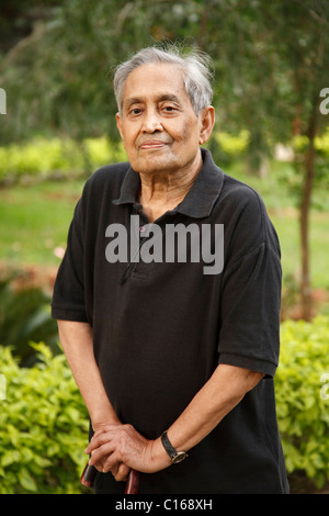 Elderly Indian Asian man stands in a park with a walking stick Stock Photo