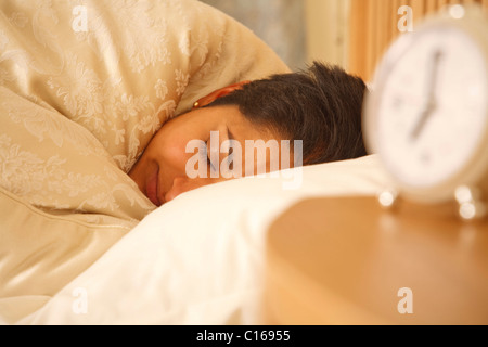 Young Indian woman sleeping in a bed with an alarm clock in the foreground Stock Photo