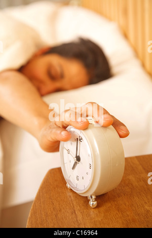 An Indian Asian woman wakes up to turn off a traditional alarm clock Stock Photo