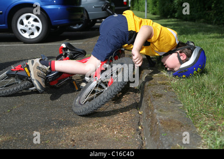 Five-year-old boy wearing a bicycle helmet falling off his bicycle, posed photo Stock Photo