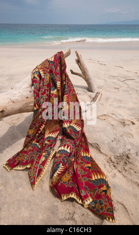 A batik sarong draped over driftwood log on the beach at Bias Tegal in Padang Bai Bali Indonesia Stock Photo