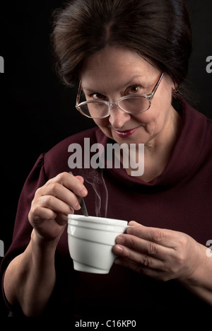 Smiling woman in glasses holding cup of hot drink. Studio portrait on dark background Stock Photo