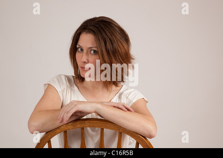 a pretty woman  leaning on the back of a wooden chair with eye contact showing a serious and thoughtful expression Stock Photo