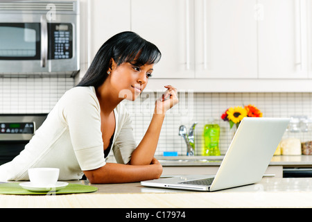 Thoughtful black woman using computer in modern kitchen interior Stock Photo