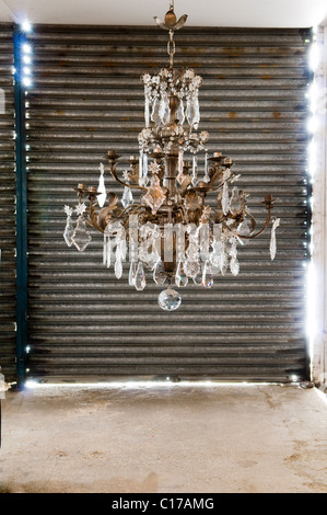 Ornate chandelier with glass and metalwork set against metal shutters of storeroom warehouse Stock Photo