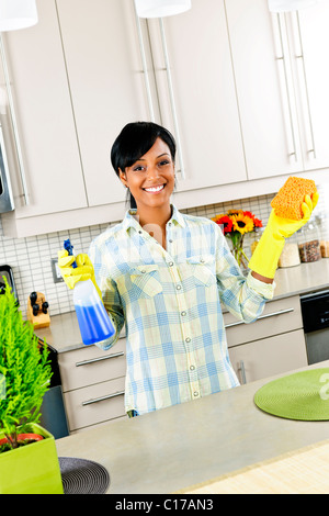 Smiling young black woman with sponge and rubber gloves cleaning kitchen Stock Photo